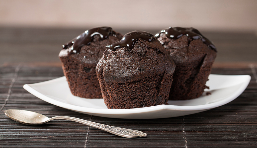 Chocolate cupcakes are displayed on a white plate with a silver spoon set to the left side of the plate